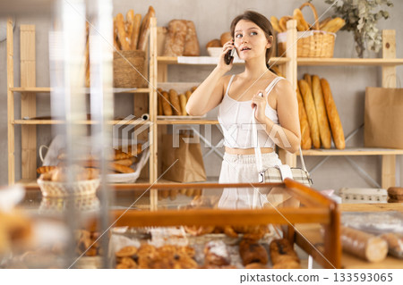 Young girl is talking on a mobile phone - asking for advice on what kind of pastries to buy for breakfast Young girl is talking on a mobile phone - asking for advice on what kind of pastries to buy for breakfast 133593065