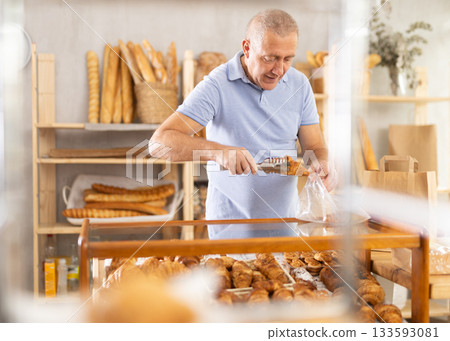 European senior man visitor puts croissant in plastic disposable bag European senior man visitor puts croissant in plastic disposable bag 133593081