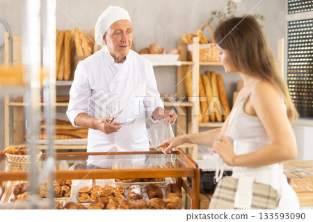 Girl selects and buys hot croissants at a bakery. Male salesperson places croissants in plastic bag 133593090