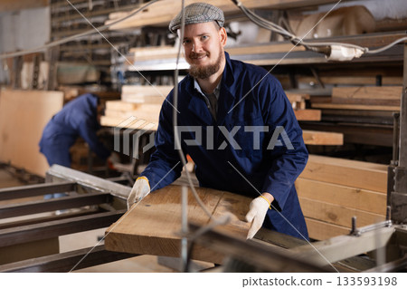 Male worker carries board from storage location to processing location. Selects planks for furniture manufacture 133593198