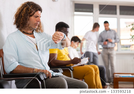 Man looking at watch while sitting in lobby of medical clinic 133593218