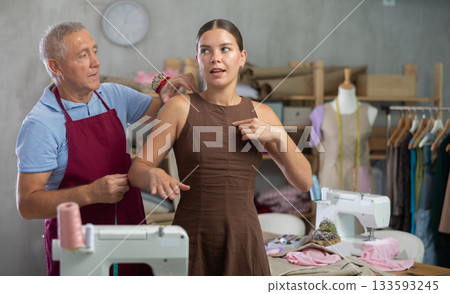 Elderly man tailor takes body measurements from young woman 133593245