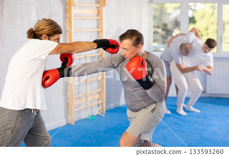 Two men in group boxing classes practicing sparring technique of blowing to body in gym Two men in group boxing classes practicing sparring technique of blowing to body in gym 133593260