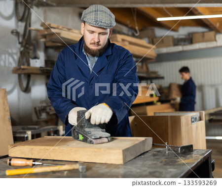 Young man polishing wooden board in workshop Young man polishing wooden board in workshop 133593269