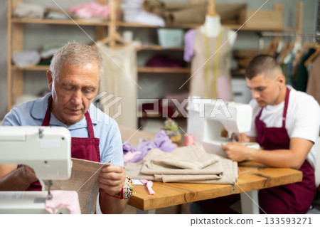 Elderly and young man sew on machine in workshop 133593271