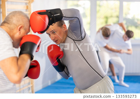 Man with old man practicing boxing blow to head in sport club Man with old man practicing boxing blow to head in sport club 133593273