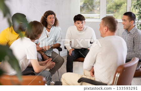 Group of guys engaged in discussion sitting on chairs in circle Group of guys engaged in discussion sitting on chairs in circle 133593291