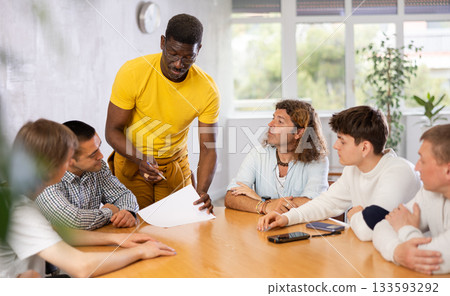 Middle-aged man instructor explaining the topic to group of guys around the table Middle-aged man instructor explaining the topic to group of guys around the table 133593292