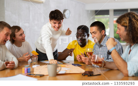 Group of enthusiastic men playing board game sitting around table Group of enthusiastic men playing board game sitting around table 133593293