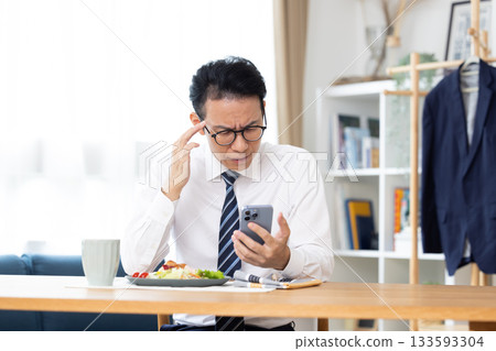 A man eating while looking at his smartphone before going to work A man eating while looking at his smartphone before going to work 133593304