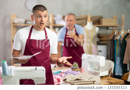 Elderly male tailor scolding assistant with document for dismissal 133593313