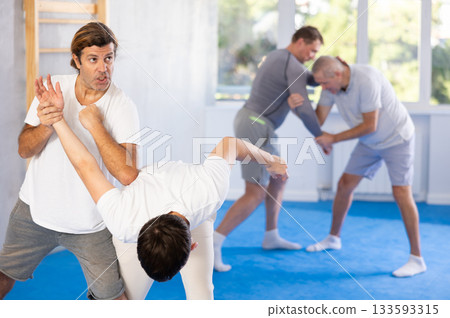 Young guy and man practice wrestling, apply techniques of Aikido and self-defense. Young guy and man practice wrestling, apply techniques of Aikido and self-defense. 133593315