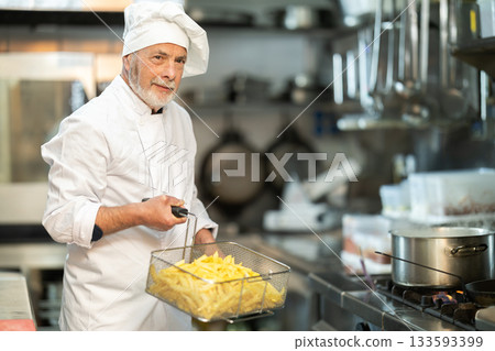 Senior male cook carrying potato slices in container Senior male cook carrying potato slices in container 133593399