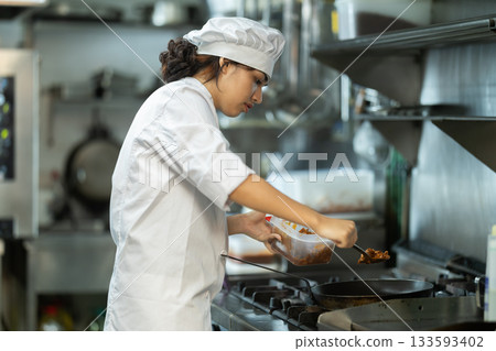 Young female cook frying ingredients in restaurant kitchen 133593402