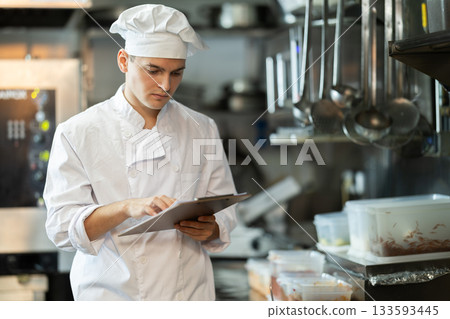 Young male chef conducts inspection in restaurant kitchen Young male chef conducts inspection in restaurant kitchen 133593445