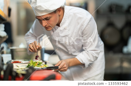 Young male cook preparing salad for service in restaurant kitchen Young male cook preparing salad for service in restaurant kitchen 133593462