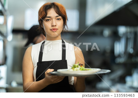 Young female waitress with prepared dish in restaurant kitchen Young female waitress with prepared dish in restaurant kitchen 133593463