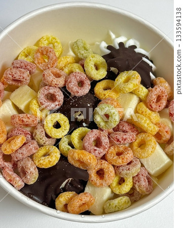 Swirled yogurt ice cream dessert served in a cup, smooth creamy texture with glossy surface, topped with fresh fruit pieces, highlighting its refreshing and inviting appearance in detail 133594138