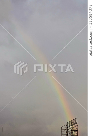 A vibrant rainbow arching across the sky after rain, with its vivid spectrum of colors creating a breathtaking and serene natural view against the clouds. 133594375