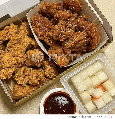 Golden crispy fried chicken served alongside bright yellow pickled radish slices, showing crunchy texture, juicy meat, and vibrant contrast of colors on a clean plate in close-up detail 133594445