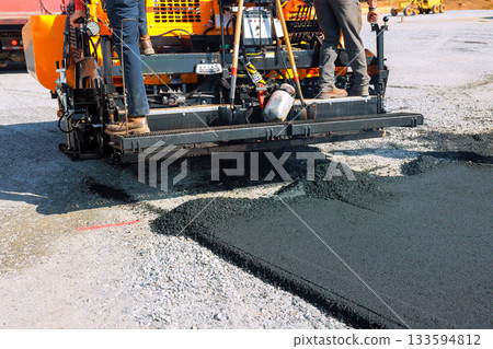 Workers operate paving machine to lay new asphalt on construction road site Workers operate paving machine to lay new asphalt on construction road site 133594812