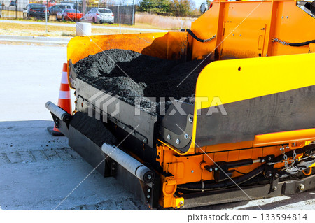 Heavy machinery spreads hot asphalt for road paving in bustling city environment. Heavy machinery spreads hot asphalt for road paving in bustling city environment. 133594814