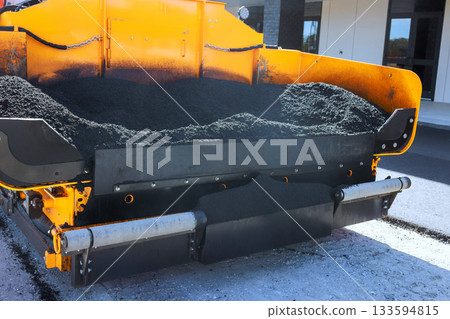 Heavy paving machinery pours fresh hot asphalt onto road at construction site smooth surface. 133594815