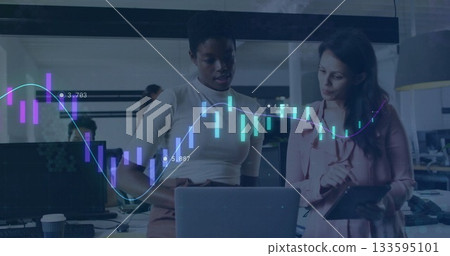 Collaborating female professionals in office attire analyzing charts in office, with laptop, tablet 133595101