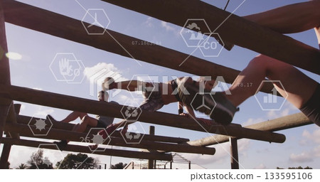Balancing female athlete carrying medicine ball stepping on wooden beam in outdoor fitness park 133595106