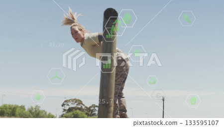 Female soldier in camouflage and tan top climbing post in training field, with hexagonal overlays 133595107