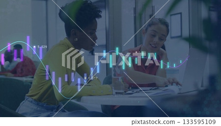Two female coworkers pointing at charts while typing on laptops in office lounge, financial overlay Two female coworkers pointing at charts while typing on laptops in office lounge, financial overlay 133595109