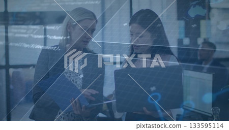 Pointing two women in blazers holding laptop, reviewing blue folder at office with digital graphic Pointing two women in blazers holding laptop, reviewing blue folder at office with digital graphic 133595114