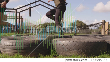 Navigating woman wearing sportswear stepping onto tire on outdoor obstacle run, with hanging ropes Navigating woman wearing sportswear stepping onto tire on outdoor obstacle run, with hanging ropes 133595133