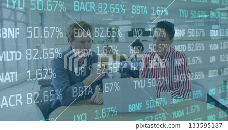 Reviewing data on laptop two professionals collaborating in open office, with stock ticker graphics 133595187
