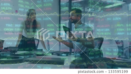 Collaborating colleagues reviewing data on tablets and laptops in meeting room, with stock charts Collaborating colleagues reviewing data on tablets and laptops in meeting room, with stock charts 133595199