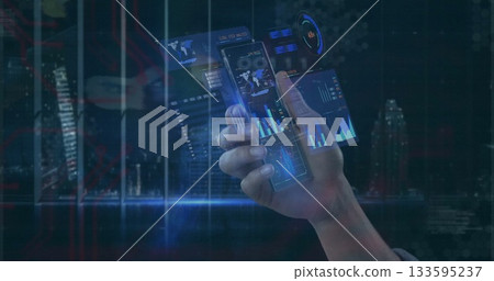 Gripping human hand projecting holographic charts above urban night skyline, with smartphone panels 133595237