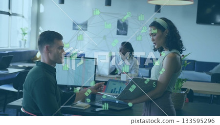 Professionals collaborating at desk in office, reviewing data visualization on monitor and laptop 133595296