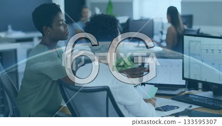 Two African American women pointing at monitor and holding documents in office, with dual monitors Two African American women pointing at monitor and holding documents in office, with dual monitors 133595307