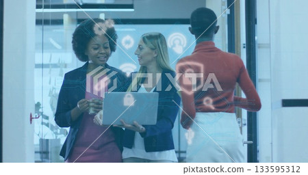 Standing three businesswomen holding laptop and smartphone by glass door in office hallway 133595312