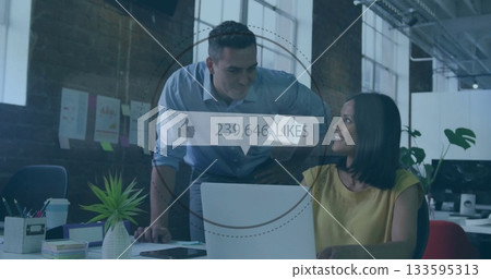 Leaning man and seated woman discussing printed charts at office, with laptop and likes overlay 133595313
