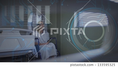 Sitting woman patient wearing gown in ward, with wheelchair, rails, stethoscope and digital overlay 133595325