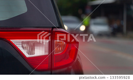 Tarillight of black car driving on the road. Speed light of car from brake. Blurred of traffic police on the road signaling cars to stop. Environment at evening or morning. Tarillight of black car driving on the road. Speed light of car from brake. Blurred of traffic police on the road signaling cars to stop. Environment at evening or morning. 133595928