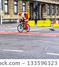 A person dressed as Santa Claus is riding a bicycle on a city street 133596323