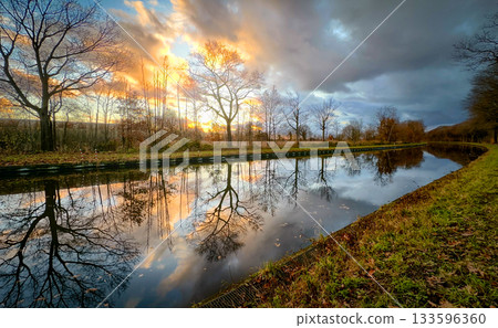 A Serene Sunset Reflection Over a Beautiful Tranquil River Landscape at Dusk, casting a warm glow A Serene Sunset Reflection Over a Beautiful Tranquil River Landscape at Dusk, casting a warm glow 133596360