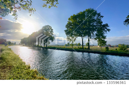 A picturesque and serene river landscape featuring lush green trees illuminated by a golden sunset 133596361