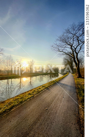 Beautiful Scenic Canal Path at Sunrise with Calm and Clear Reflections in the Water Beautiful Scenic Canal Path at Sunrise with Calm and Clear Reflections in the Water 133596362