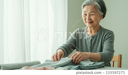 Happy senior woman enjoys folding laundry. A simple happy life, happy moments Happy senior woman enjoys folding laundry. A simple happy life, happy moments 133597271