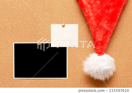 Blank paper notes and an empty photo are pinned to a cork board. Santa's hat on a cork board 133597610