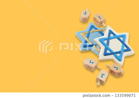 Hanukkah stars of David and wooden dreidels arranged on yellow 133599071