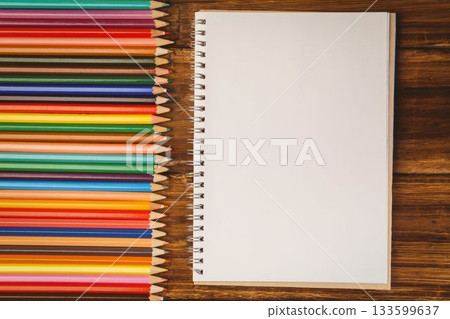 Flat lay illustration is showing spiral-bound notebook with colored pencils on wooden desk 133599637